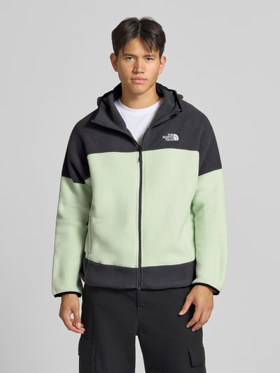 Männermodel trägt Fleecejacke mit Kapuze und Logo-Stitching von The North Face in Mintgrün und Schwarz, Struktur Fleece, Reißverschluss, Ganzkörperansicht von vorne.