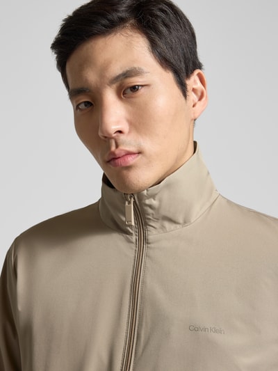 Männermodel trägt Jacke mit Stehkragen und Reißverschluss von Calvin Klein in Beige, glatte Oberfläche, Nahaufnahme Oberkörper, Regular Fit.