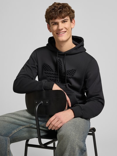 Männermodel trägt Hoodie mit Kapuze von adidas Originals, schwarze Baumwoll-Mix-Optik, lockerer Schnitt, Label-Print, Nahaufnahme Oberkörper.
