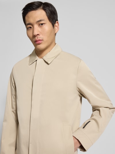 Mężczyznamodel nosi jasnobeżowy Kurzmantel mit Umlegekragen und Label-Detail Modell 'EIDE' von Casual Friday, materiał z domieszką stretchu, krój regular fit, z kieszeniami, detailowe ujęcie górnej części ciała, Nahaufnahme Oberkörper.