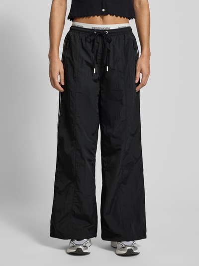 Kobieta prezentuje Spodnie typu track pants Regular Fit Trackpants mit Kontraststreifen od Tommy Jeans, efekt: jednolity kolor, krój regular fit, aplikacja: paski w kontrastowym kolorze, pas z logo, tunel, ściągacz: elastyczny, dwie warstwy pasa, boczne kieszenie zapinane na zamek błyskawiczny, kieszeń z tyłu, całkowity widok z przodu