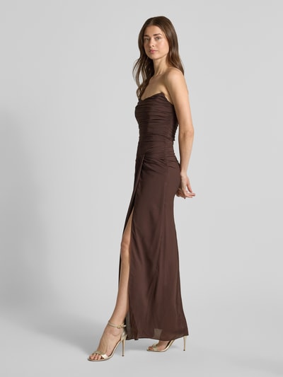 Frauenmodel trägt Cocktailkleid im Off-Shoulder-Look Modell 'Arli' von Forever New, Material-Mix mit Stretch-Anteil, Drapierungen, Knotendetail, figurbetonter Schnitt, Maxikleid, braun, glatte Textur, Ganzkörperansicht von vorne.