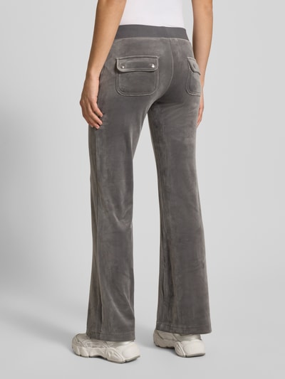 Frauenmodel trägt Low Rise Sweatpants mit elastischem Bund Modell 'LAYLA' von Juicy Couture aus grauem, weichem Baumwoll-Mix mit Stretch-Anteil, Flared-Cut, aufgesetzte Eingrifftaschen, samtiger Textur, Ganzkörperansicht Rückansicht.
