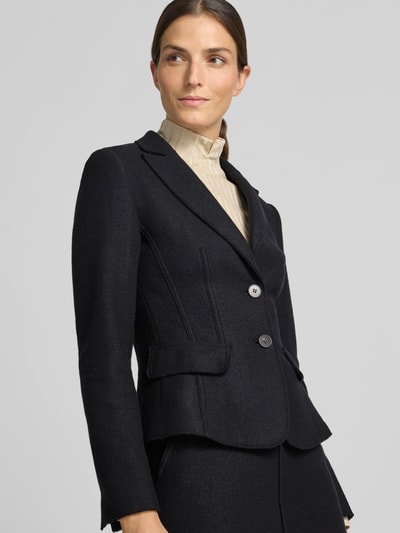 Frauenmodel trägt Slim Fit Kurzblazer aus reiner Schurwolle von Marc Cain in Schwarz mit Reverskragen, Knopfverschluss und Pattentaschen, Nahaufnahme Oberkörper. Rückenlänge, Brustweite und Ärmellänge bei Größe 36.