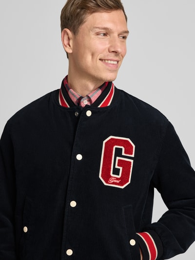 Männermodel trägt College-Jacke aus Cord mit Label-Detail von Gant, reine Baumwolle, Regular-Fit, Dunkelblau, Nahaufnahme Oberkörper.