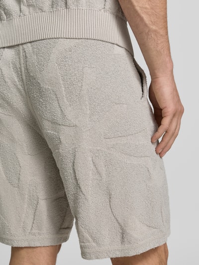 Männermodel trägt Regular Fit Sweatshorts aus Baumwoll-Mix Modell 'ASURFER' von BOSS Orange mit Optik: Unifarben, Struktur, Label-Patch, Bundabschluss: elastisch mit Tunnelzug, Eingrifftaschen, Materialverarbeitung: Frottee, Farbe Beige, Nahaufnahme Rückansicht.