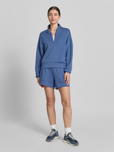 Frauenmodel trägt Shorts mit Eingrifftaschen Modell 'atrium' von VARLEY, Viskose-Mix mit Stretch-Anteil, High-Rise-Fit, elastischer Bund mit Kordelzug, Farbe mittelblau, glatte Textur, Ganzkörperansicht von vorne.