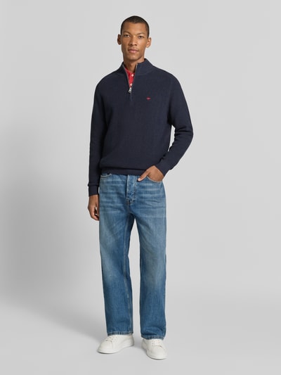 Męski model nosi Regular Fit Strickpullover aus reiner Baumwolle mit Troyer-Kragen od Fynch-Hatton, granatowy kolor, imitacja dzianiny, wyhaftowane logo, krój z długim rękawem, prążkowane wykończenia; długość tyłu w rozmiarze M: 65 cm, długość rękawów: 75 cm, całkowity widok z przodu.