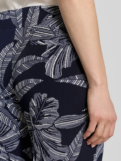 Männermodel trägt Hose im Allover-Look mit Eingrifftaschen von Vera Mont, ciemny granat z białym wzorem liści, materiał z domieszką stretchu, szeroka nogawka, Szerokość w rozmiarze 36: 39 cm, długość nogawki wewnętrznej 84 cm, Nahaufnahme biodra