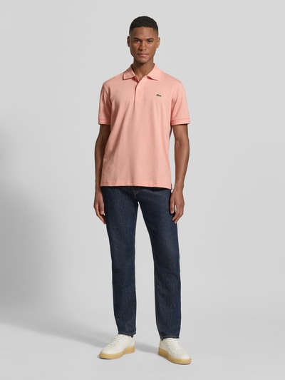 Männermodel trägt Regular Fit Poloshirt aus Baumwoll-Mix von Lacoste in Rosa, unifarben, Logo-Detail, Piqué-Textur, Ganzkörperansicht von vorne.