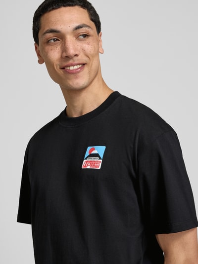 Męski model nosi T-Shirt mit Label-Print Modell 'SUNSET ON FUJI SAN' od Edwin, czarna bawełna, krój relaxed fit, dekolt okrągły, zbliżenie na górną część ciała.