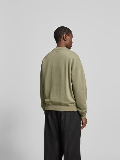 Männermodel trägt Oversized Sweatshirt aus Baumwolle von Anine Bing in Olive mit Label-Detail, elastische Abschlüsse, Rückenlänge 61 cm, Ganzkörperansicht Rückansicht.