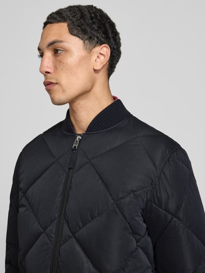 Männermodel trägt Regular Fit Steppjacke mit opstaande kraag van Superdry, zwarte Stiksels, ritssluiting, Nahaufnahme Oberkörper. Context: Heren gewatteerd jack, steekzakken, elastische mouwboorden, ruglengte maat M 69 cm, schouderbreedte 46 cm, borstwijdte 58 cm, mouwlengte 59 cm.