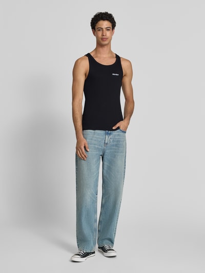 Männermodel trägt Tanktop in Ripp-Optik mit Logo von REVIEW in Schwarz, Slim-Fit, Reine Baumwolle, Rundhalsausschnitt, Ganzkörperansicht von vorne. Rückenlänge bei Größe M: 67 cm.