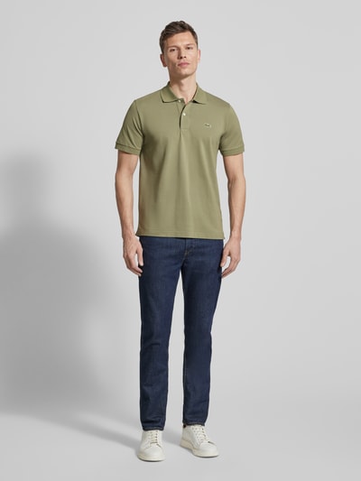 Männermodel trägt Regular Fit Poloshirt aus Baumwoll-Mix von Lacoste in Olivgrün mit Logo-Detail, Piqué-Struktur, Ganzkörperansicht von vorne.