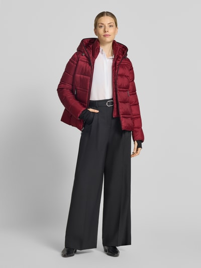 Frauenmodel trägt Steppjacke mit Kapuze und Reißverschlusstaschen von MICHAEL Michael Kors in Rot, seitliche Reißverschlusstaschen, Elastiksaum, gerader Schnitt, Steppnähte, Ganzkörperansicht von vorne.