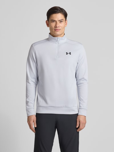 Männermodel trägt Sweatshirt mit Label-Detail von Under Armour in Hellgrau, lockerer Schnitt, Stehkragen, Reißverschluss, gerippte Abschlüsse, Rückenlänge 72 cm, Ärmellänge 67 cm, Ganzkörperansicht von vorne.
