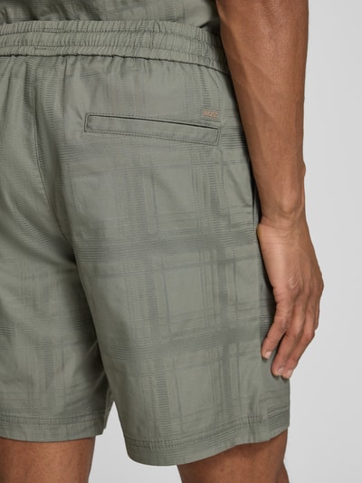 Männermodel trägt Tapered Chinoshorts aus reiner Baumwolle Modell 'SANDREW_6_SHORTS' von BOSS Orange in Olivgrün mit Strukturmuster, elastischer Bund, Seitenschlitz am Beinabschluss, unifarbene Optik, Detailaufnahme Rückansicht.