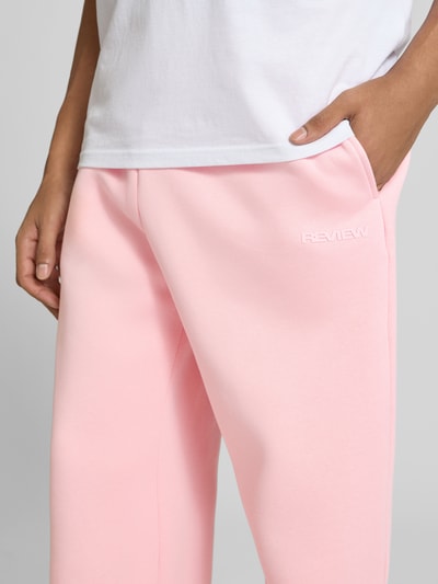 Männermodel trägt Straight Fit Sweatpants Baumwoll-Mix von REVIEW in Rosa, Label-Print, seitliche Eingrifftaschen, Nahaufnahme Oberschenkel.