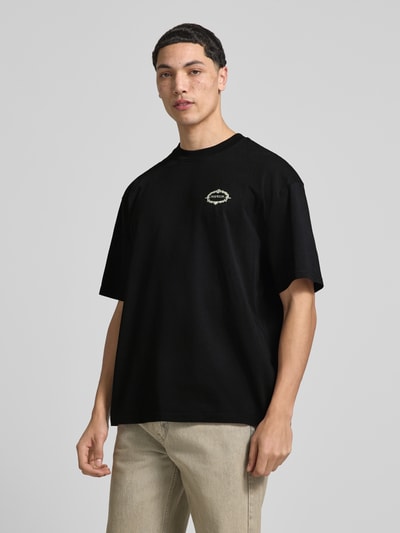 Männermodel trägt Oversized T-Shirt mit rückseitigem Motiv-Print Modell 'Reine' von Pegador aus Reine Baumwolle, Label-Print, Oversized-Fit, Rundhalsausschnitt, Herren T-Shirt, Rückenlänge bei Größe M 70 cm, schwarze Farbe, glatte Textur, Ganzkörperansicht von vorne.