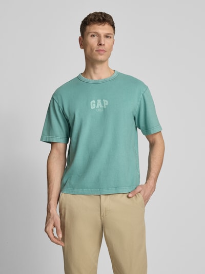 Männermodel trägt T-Shirt mit Logo und Rundhalsausschnitt von GAP in Türkis, Reine Baumwolle, Regular-Fit, Rückenlänge 61 cm, Ganzkörperansicht von vorne.