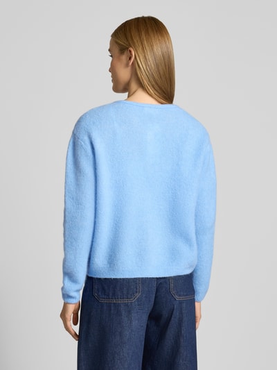 Frauenmodel trägt Strickjacke mit Knopfleiste Modell 'VITOW' von American Vintage in Hellblau, lockerer Schnitt, gerippte Abschlüsse, Ganzkörperansicht Rückansicht.
