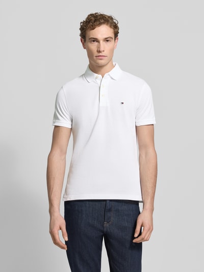 Männermodel draagt Slim Fit Poloshirt met Stretch-Anteil van Tommy Hilfiger, mix van katoen en elastaan, polokraag, geborduurd logo, geheel wit, korte mouwen, knoopsluiting, ruglengte maat M 69 cm, recht vooraanzicht bovenlichaam.