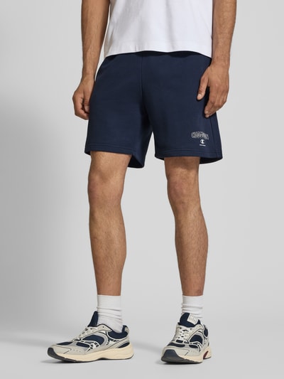 Männermodel trägt dunkelblaue Sweatshorts mit Logo und elastischem Bund von CHAMPION aus Baumwoll-Mix, Regular-Fit, Nahaufnahme Oberschenkel.