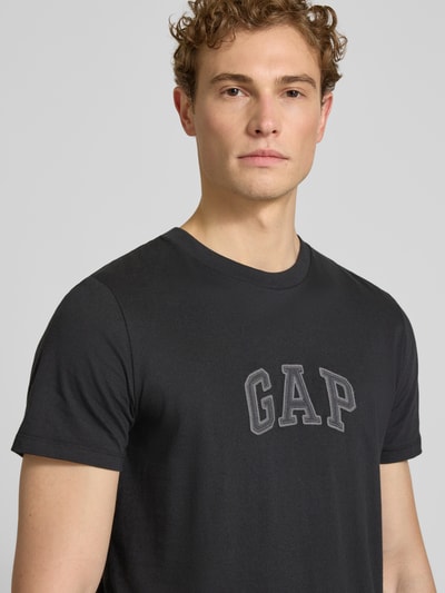 Männermodel trägt T-Shirt mit Logo-Patch und Rundhalsausschnitt von GAP in Schwarz, reine Baumwolle, Straight Fit, Nahaufnahme Oberkörper.