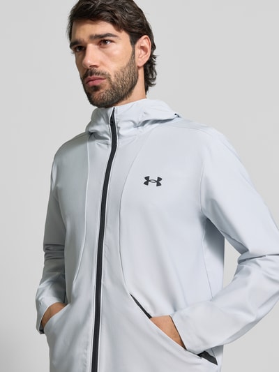 Männermodel trägt Regular Fit Jacke mit Logo-Print Modell 'Unstoppable' von Under Armour in Hellgrau, Elastischer-Material-Mix, Nahaufnahme Oberkörper