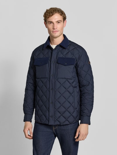Männermodel trägt Regular Fit Jacke in Stepp-Optik Modell 'FIRMIN' von Save The Duck in Dunkelblau, Brusttaschen, Umlegekragen, Ganzkörperansicht von vorne.