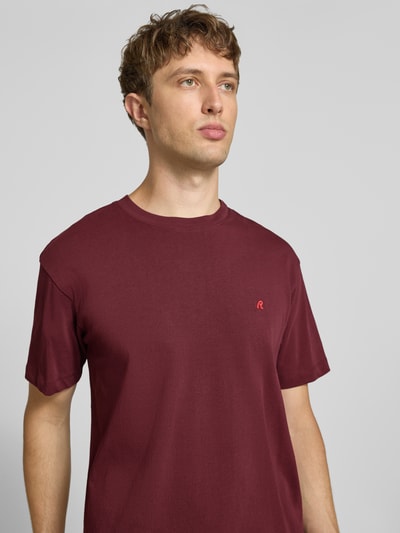 Männermodel trägt Regular Fit T-Shirt aus reiner Baumwolle von Replay in Dunkelrot, dezente Label-Stickerei, Nahaufnahme Oberkörper.