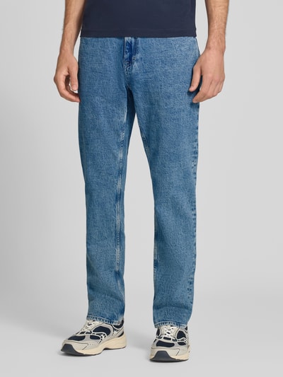 Męski model nosi Slim Straight Fit Jeans aus Baumwoll-Mix Modell 'RYAN' von Tommy Jeans, niebieski denim, prosta nogawka, tekstura gładka, kontekst: Herren Bomberjacke / blouson von Tommy Jeans, zdjęcie całej sylwetki z przodu.