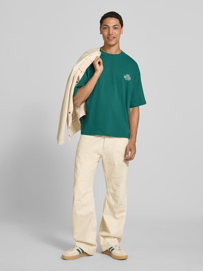 Männermodel trägt Oversized T-Shirt mit rückseitigem Print von REVIEW, Herren T-Shirt im Oversized-Fit aus Bio-Baumwoll-Mix, Rundhalsausschnitt, Logo-Print, Rückenlänge bei Größe M 68 cm, Ganzkörperansicht von vorne.
