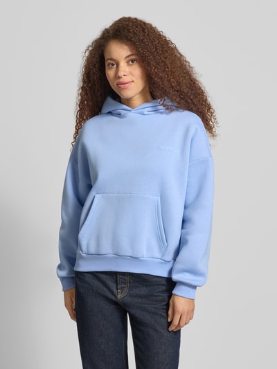 Frauenmodel trägt Hoodie mit Logo und Känguru-Tasche von Review in Hellblau, Baumwoll-Mix, Relaxed Fit, Ganzkörperansicht von vorne.