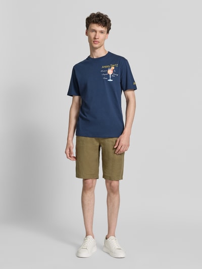 Männermodel trägt ein dunkelblaues Herren T-Shirt mit Stitchings Modell 'PORTOFINO' von MC2 Saint Barth aus reiner Baumwolle, Regular-Fit, Rundhalsausschnitt, kombiniert mit olivgrüner Shorts und weißen Sneakers, Ganzkörperansicht von vorne.