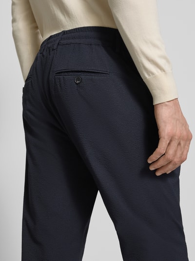 Mężczyzna nosi Slim Fit Stoffhose mit Strukturmuster od CRUNA, elastyczna mieszanka materiałów, krój slim fit, fakturowany wzór, wpuszczane kieszenie, kieszeń z tyłu, elastyczny pas, szerokość w rozmiarze 50: 44 cm, długość wewnętrzna nogawki w rozmiarze 50: 79 cm, ciemny kolor, fakturowana powierzchnia, widok tylnej części spodni, zbliżenie na pośladki i pas, detal