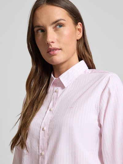 Frauenmodel trägt Hemdbluse aus Baumwolle mit Streifenmuster von GANT in Rosa mit durchgehender Knopfleiste, Nahaufnahme Oberkörper.
