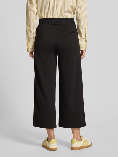 Vrouwenmodel draagt Stoffhose met Eingrifftaschen van ICHI, zwarte unikleuren, losse pasvorm, elastische taille, volledig beeld achteraan.