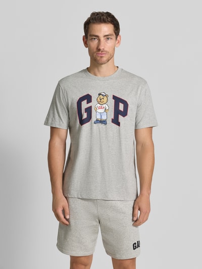 Męski model nosi Regular Fit T-Shirt mit Logo-Print von GAP z bawełny, okrągły dekolt, szary, długość tyłu 62 cm, Ganzkörperansicht von vorne.