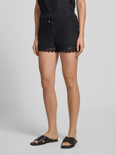 Frauenmodel trägt Regular Fit Sweatshorts mit Spitze Modell 'HONEY' von Vero Moda, Optik: Unifarben, Spitzen-Muster, Tunnelzug, Bundabschluss: Elastisch, Materialverarbeitung: Spitze, Material: Baumwoll-Mix, schwarze Farbe, leicht strukturierte Oberfläche, Ganzkörperansicht von vorne.