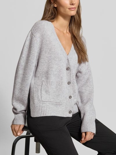 Frauenmodel trägt Strickjacke aus Woll-Mix mit Kaschmir-Anteil von MYON in hellgrau, lockere Passform, gerippte Abschlüsse, Nahaufnahme Oberkörper.
