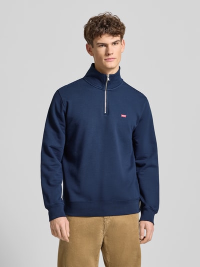 Männermodel trägt Regular Fit Troyer aus reiner Baumwolle von Levi's®, dunkelblau, Stehkragen, kurzer Reißverschluss, Label-Detail, gerippte Abschlüsse, Rückenlänge 72 cm, Ärmellänge 70 cm, Ganzkörperansicht von vorne