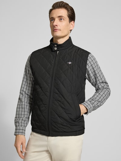 Männermodel trägt Regular Fit Weste mit Stehkragen in Stepp-Optik von Gant, schwarz, Logo-Stitching, Reißverschluss, Ganzkörperansicht von vorne.