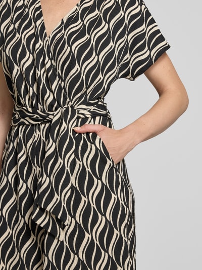 Frauenmodel trägt Jumpsuit im Allover-Look mit V-Ausschnitt von Betty Barclay, schwarz-beige Muster, Material-Mix mit Stretch, Nahaufnahme Oberkörper.