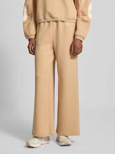 Frauenmodel trägt Wide Fit Sweatpants aus Baumwoll-Mix Modell 'Gunda' von GUIDO MARIA KRETSCHMER WOMAN in Beige mit Logo-Print, elastischem Bund, und Eingrifftaschen, Nahaufnahme Unterkörper, Kontext: elastischer Baumwoll-Mix, Wide Fit, Modell 'Gunda', Logo-Print, Tunnelzug, Bundweite 38 cm, Innenbeinlänge 76 cm.