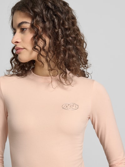 Frauenmodel trägt Slim Fit Longsleeve mit Logo-Detail von ANOTHER COTTON LAB, elastischer Baumwoll-Mix, Rundhalsausschnitt, Nahaufnahme Oberkörper.