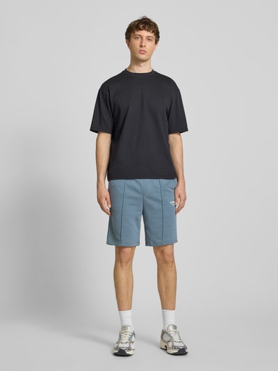 Męski model nosi Sweatshorts mit Logo Model 'KANE' od Jack & Jones, mieszanka bawełny, krój relaxed fit, niebieski kolor, elastyczny pas, logo, Szerokość w rozmiarze M: 42 cm, długość nogawki wewnętrznej 19 cm, widok całej sylwetki z przodu.
