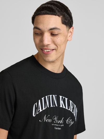 Männermodel trägt T-Shirt mit Label-Stitching von Calvin Klein Jeans in Schwarz, Reine Baumwolle, Slim-Fit, Rundhalsausschnitt, Nahaufnahme Oberkörper.