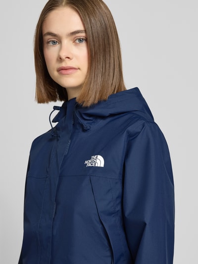 Modelka nosi Regular Fit Parka mit Logo-Print Modell 'Antora' od The North Face w kolorze granatowym, z kapturem i kieszeniami, krój regular fit, z elastycznymi mankietami; długość pleców 74 cm, szerokość w rozmiarze S: 50 cm, ramiona 39 cm, rękawy 64 cm; zbliżenie na górną część ciała.